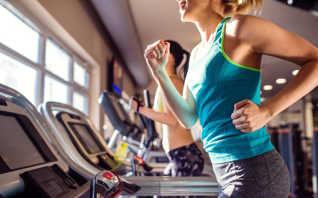 Two fit women running on treadmills in modern gym